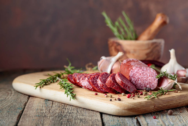 Smoked salami on a old wooden table. Sausages with rosemary , garlic and pepper. - Photo, Image