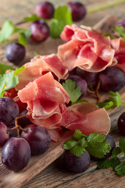 Prosciutto con perejil y uvas sobre una vieja mesa de madera. Alimento ecológico saludable
 .  - Foto, Imagen