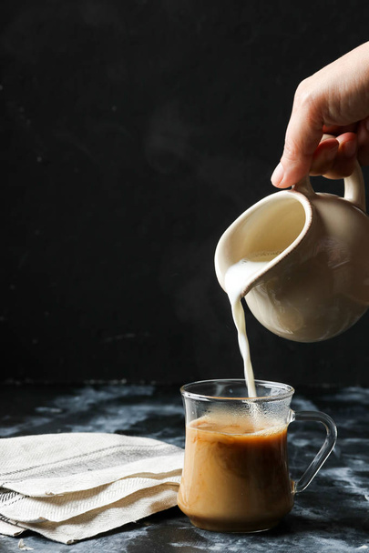 Woman hand pouring milk into glass cup of coffee - Foto, Imagem