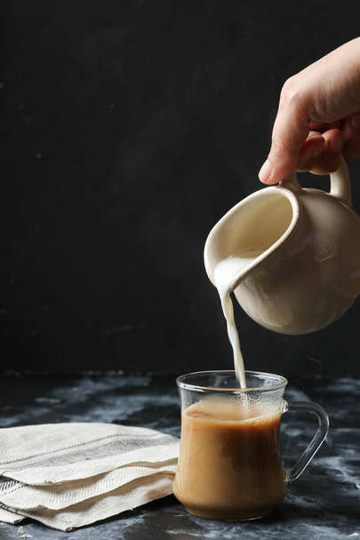 Woman hand pouring milk into glass cup of coffee - Foto, Imagem