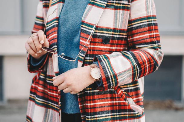 Close-up detail of fashion accessories, stylish young woman wearing an overcoat with a chequered pattern, a golden ring, a pair of modern sunglasses and a wrist watch. - Foto, Imagem