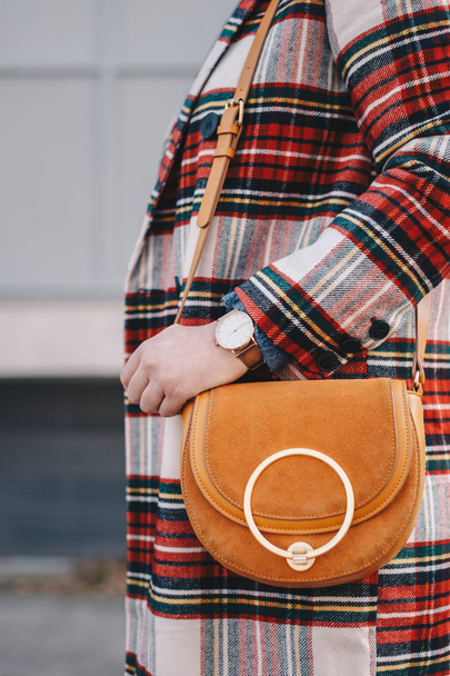 Zbliżenie na szczegóły moda, stylowe młoda kobieta na sobie płaszcz z wzorzec tartan i zegarek na rękę trzymając fantazyjny żółty worek. - Zdjęcie, obraz