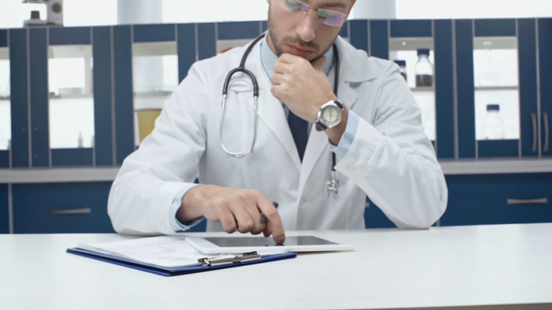 male doctor in white coat using digital tablet and writing diagnosis in clinic - Video