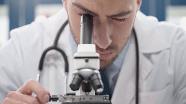 фокусированный ученый в белом халате, смотрящий в микроскоп в лаборатории
 - Кадры, видео