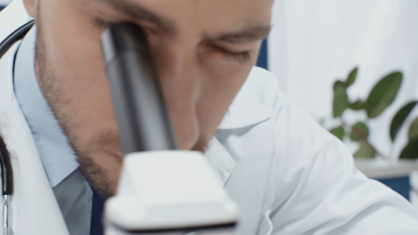 зосереджений чоловічий вчений у білому пальто, який дивиться через мікроскоп в лабораторії
 - Кадри, відео