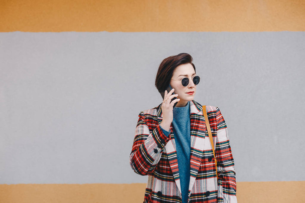 Retrato de una joven atractiva y moderna conversando por teléfono móvil, posando con ropa de moda frente a un fondo multicolor. Espacio para copia, texto y publicidad
. - Foto, imagen
