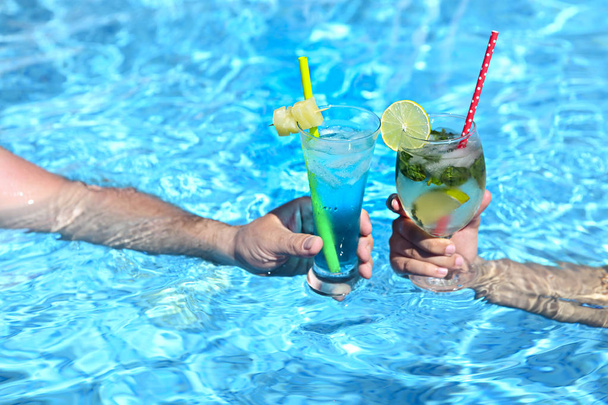 Jovem casal com copos de coquetéis de álcool mojito e lagoa azul na piscina
  - Foto, Imagem