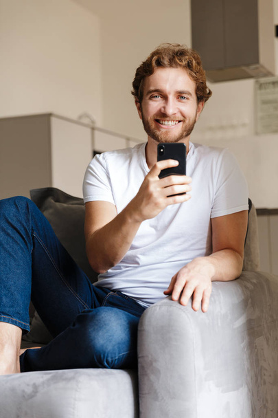 Image of a handsome young bearded man on sofa at home using mobile phone. - 写真・画像