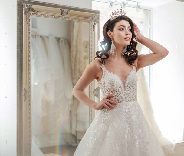 魅力的な若い花嫁は現代のウェディング サロンでウェディング ドレスを選択しながら笑っています。 - 写真・画像