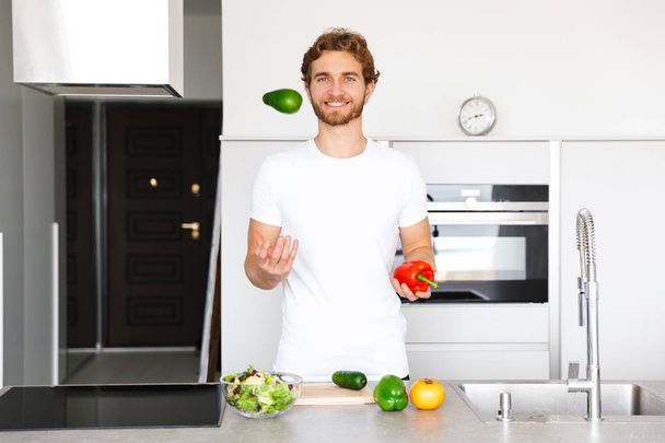 Photo of a handsome young man at kitchen at home cooking vegetables make salad. - Foto, afbeelding