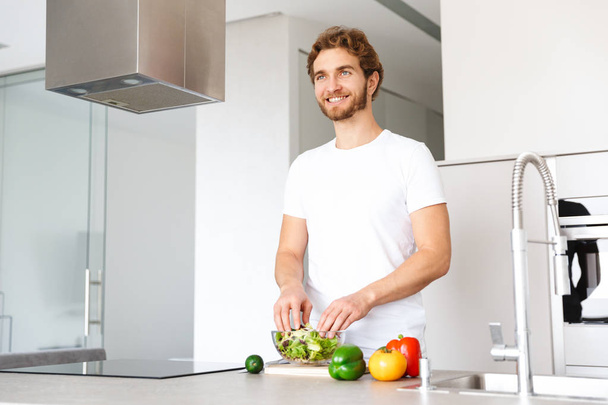 Photo of a handsome young man at kitchen at home cooking vegetables make salad. - Foto, Imagen