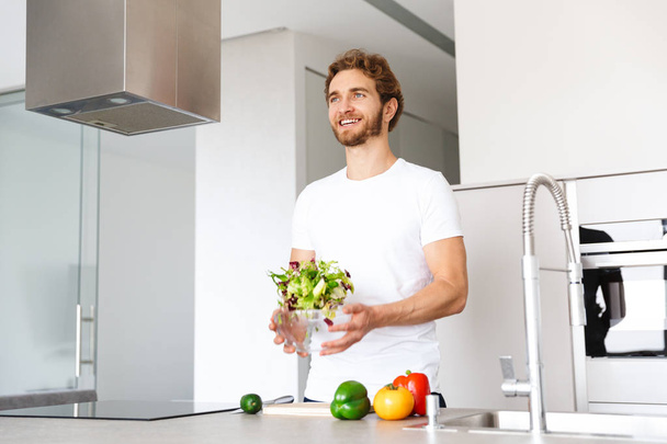 Photo of a handsome young man at kitchen at home cooking vegetables make salad. - Foto, Imagen