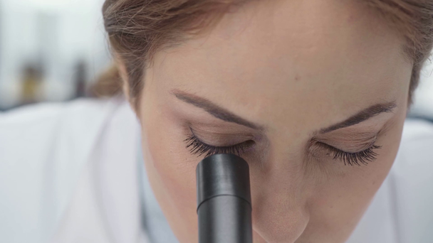 científica femenina enfocada en la capa blanca que mira a través del microscopio en laboratorio
 - Imágenes, Vídeo