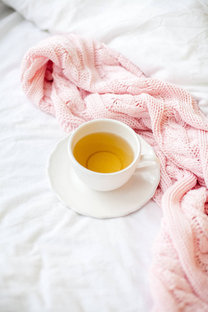 Beautiful white cup with tea on the bed, pink knitted plaid. Breakfast in bed. Morning. Spring. - Photo, Image