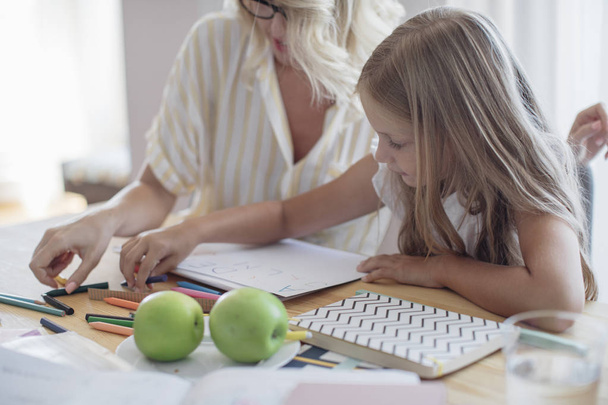 Cute Caucasian schoolgirl writing letters on paper with her mother helping. - Foto, Bild