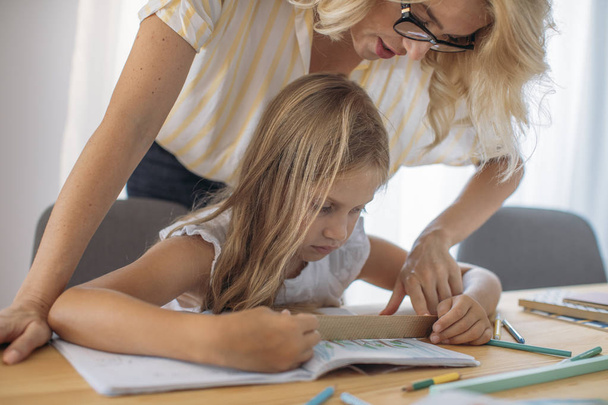 Cute blonde Caucasian girl drawing in her notebook with her mother helping. - Foto, Bild