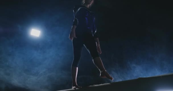 Primer plano del pie de una chica gimnasta profesional realiza un salto con rotación en la viga de equilibrio en cámara lenta. Color azul humo en el gimnasio. Concursos de gimnasia
 - Imágenes, Vídeo
