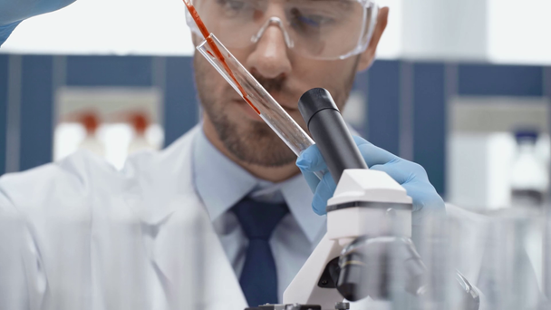 αρσενικό επιστήμονας στα γυαλιά αναζητούν μέσα από το μικροσκόπιο σε εργαστήριο - Πλάνα, βίντεο