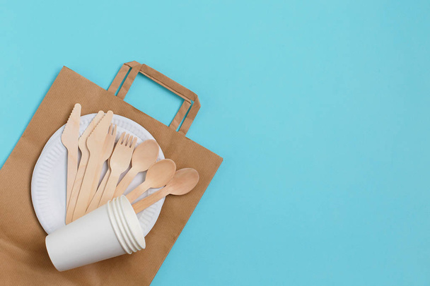 Eco-friendly disposable utensils made of bamboo wood over paper bag on blue background. - Photo, Image