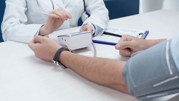 обрізаний вид жінки-лікаря, що вимірює кров'яний тиск людини з тонометром у клініці
 - Кадри, відео