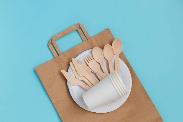 Eco-friendly disposable utensils made of bamboo wood over paper bag on blue background. - Photo, Image