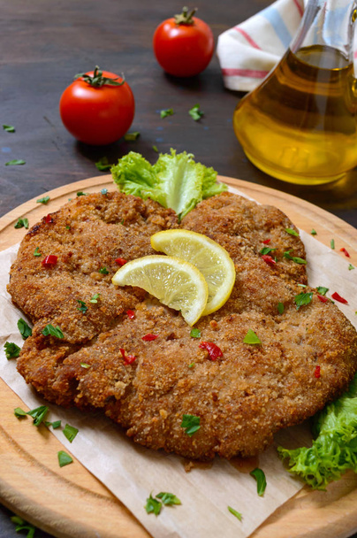 Large Viennese schnitzel on a wooden board with lemon on a dark background. Meat dish - Photo, Image