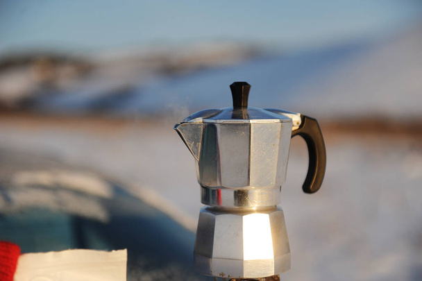 Пивоварение кофе в кофейнике мока на газовой горелке на багажнике автомобиля на открытом воздухе в зимнем российском снежном ландшафте
. - Фото, изображение