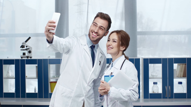 улыбающиеся женщины и мужчины врачи говорят и делают селфи на смартфоне в клинике
  - Кадры, видео