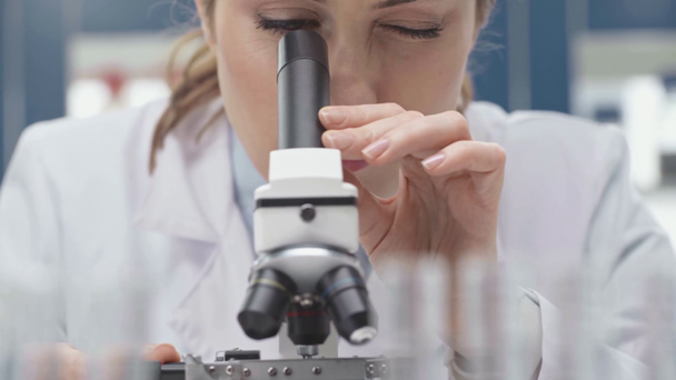 γυναίκα επιστήμονας σε λευκό παλτό ψάχνει μέσω μικροσκοπίου στο εργαστήριο - Πλάνα, βίντεο