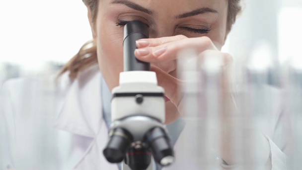 selective focus of female scientist in white coat looking through microscope in laboratory - Video