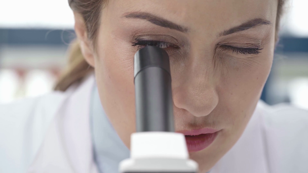 Selektivní fokus koncentrovaného ženské vědce dívá skrze mikroskop v laboratoři - Záběry, video