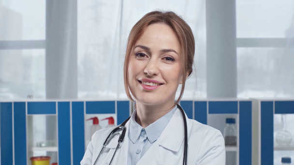 szép női orvos fehér kabátot nézett kamera klinikán mosolyogva - Felvétel, videó