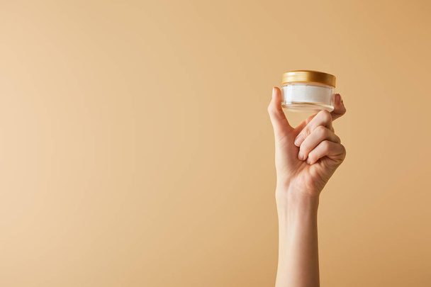 cropped view of female hand holding cosmetic cream on beige background - Fotografie, Obrázek