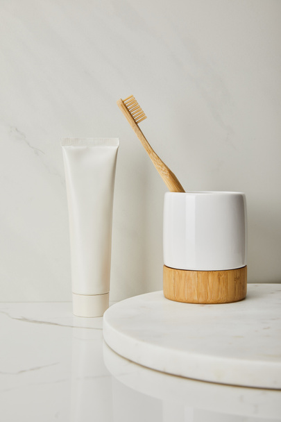 soporte con cepillo de dientes de bambú y pasta de dientes en tubo sobre fondo de mármol blanco
 - Foto, Imagen