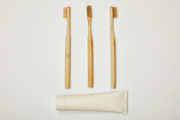 top view of toothpaste in tube and bamboo toothbrushes on white background - Φωτογραφία, εικόνα
