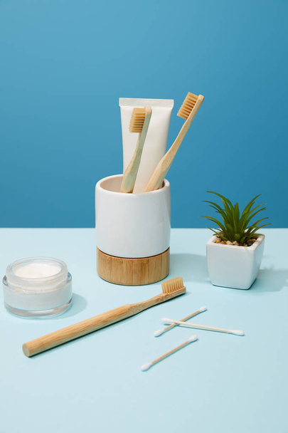 supporto con dentifricio in tubo e spazzolini in bambù, crema cosmetica e pianta in vaso su tavola e fondo blu
 - Foto, immagini
