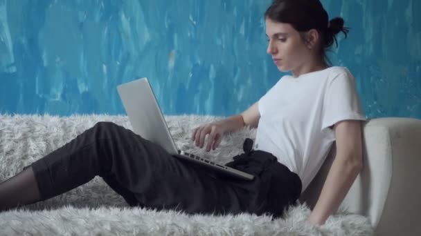 Mujer trabajando en el ordenador portátil mientras está sentado en el sofá en la habitación
. - Metraje, vídeo