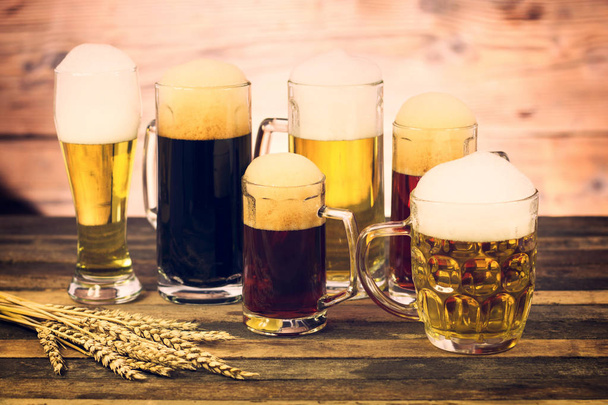 close up view of various sorts of beer in mugs on wooden surface - Foto, imagen