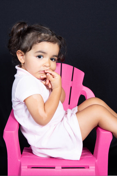 attractive kid child girl site on pink chair seat on black background - Zdjęcie, obraz