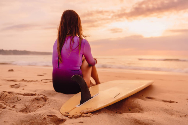 Surfer woman with surfboard on a beach at sunset or sunrise. - Foto, Imagem