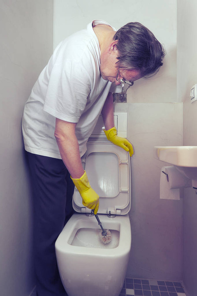 Older poor man cleaning his home with cleaner and sponge - Foto, imagen