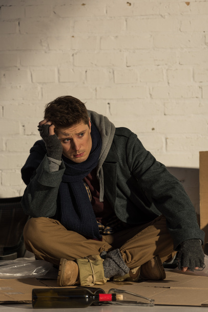 depressed homeless man sitting on cardboard and propping head with hand - Foto, imagen