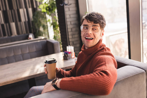 happy man in glasses holding paper cup in cafe - Foto, afbeelding