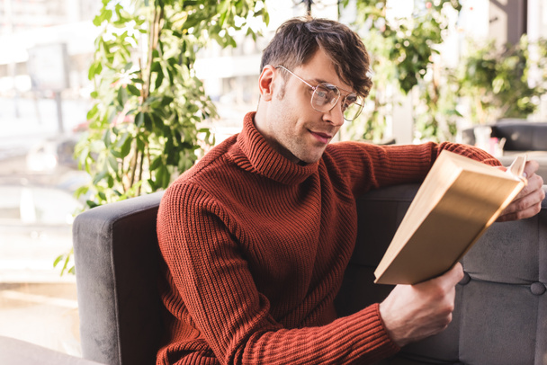 красивий чоловік в окулярах читає книгу, сидячи в кафе
 - Фото, зображення
