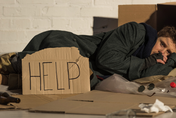 homeless poor man lying on cardboard by white brick wall - Foto, Imagen