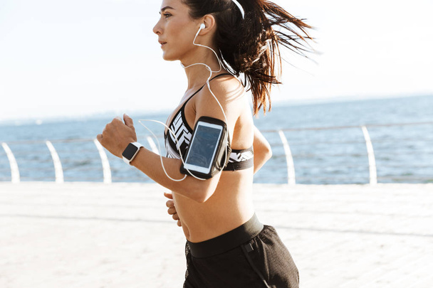Image of a beautiful young sports fitness woman running at the beach outdoors. - 写真・画像