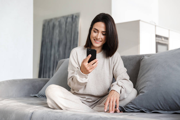 Beautiful young woman relaxing on a couch at home, using mobile phone - Φωτογραφία, εικόνα