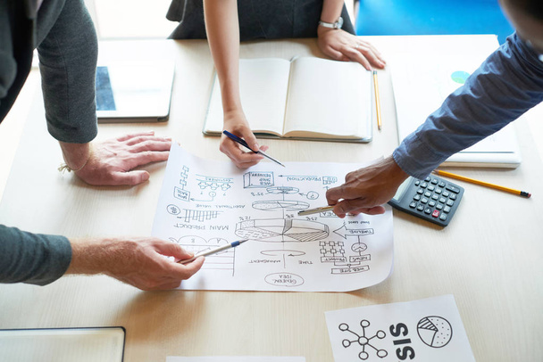 Бизнес-команда, указывающая на бизнес-план за столом во время встречи в офисе
 - Фото, изображение
