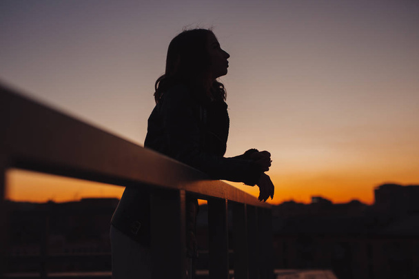 Silhouette of woman thinks and dreams about future at sunset in city - Фото, изображение