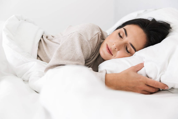 Photo of middle-aged woman 30s sleeping while lying in bed with white linen at home - Foto, Bild